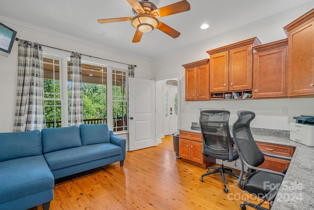 office with light wood finished floors, a ceiling fan, built in desk, and crown molding