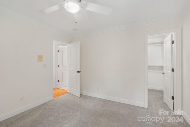 unfurnished bedroom featuring light carpet, baseboards, ornamental molding, and a walk in closet
