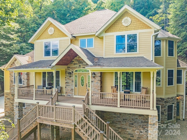 view of front of house with stone siding, a porch, roof with shingles, and stairway