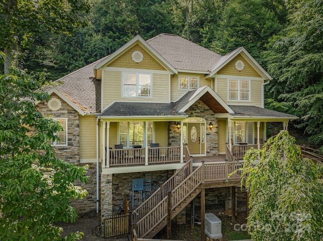 view of front of home with a porch, stone siding, roof with shingles, and stairway