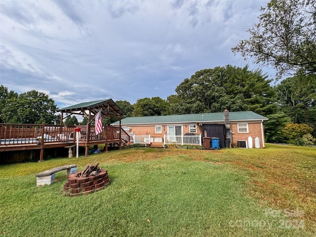 back of property with a deck, a gazebo, a fire pit, and a lawn