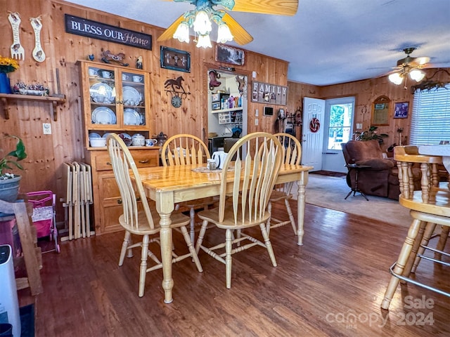 dining room with ceiling fan, wooden walls, and hardwood / wood-style flooring