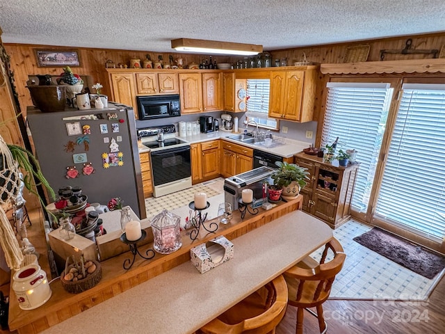 kitchen featuring electric range oven, a textured ceiling, wooden walls, sink, and stainless steel refrigerator