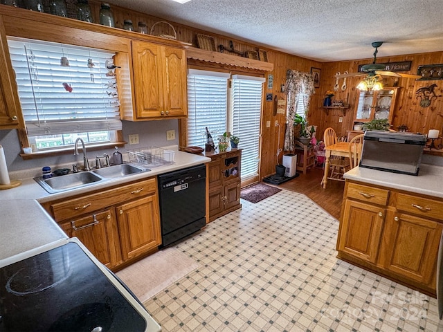 kitchen featuring pendant lighting, a textured ceiling, black dishwasher, wooden walls, and sink