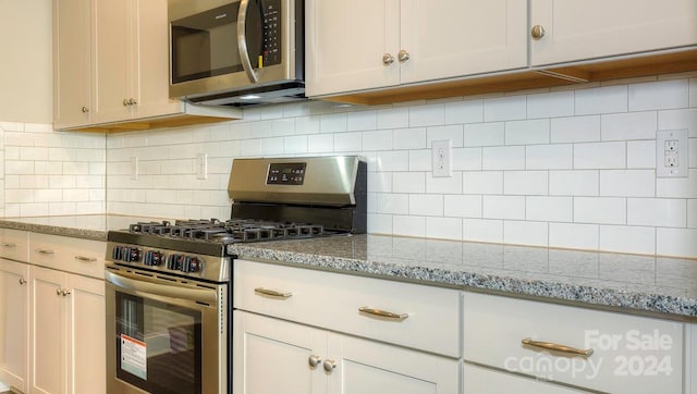 kitchen with white cabinetry, light stone countertops, backsplash, and stainless steel appliances