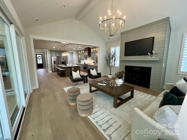 living room featuring an inviting chandelier, light hardwood / wood-style flooring, beamed ceiling, and a fireplace