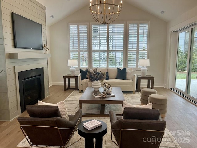 living room with an inviting chandelier, light hardwood / wood-style floors, vaulted ceiling, and a fireplace