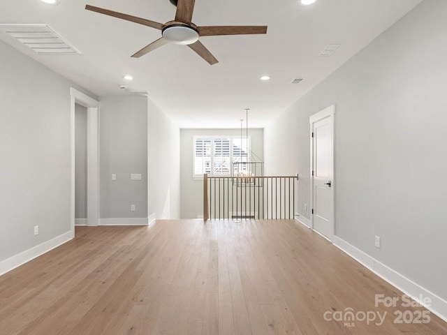 spare room featuring ceiling fan with notable chandelier and light hardwood / wood-style floors