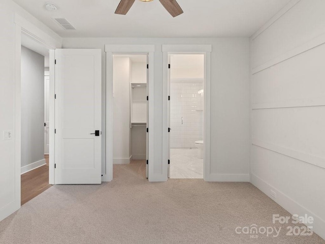 unfurnished bedroom featuring a closet, a walk in closet, ensuite bathroom, ceiling fan, and light carpet