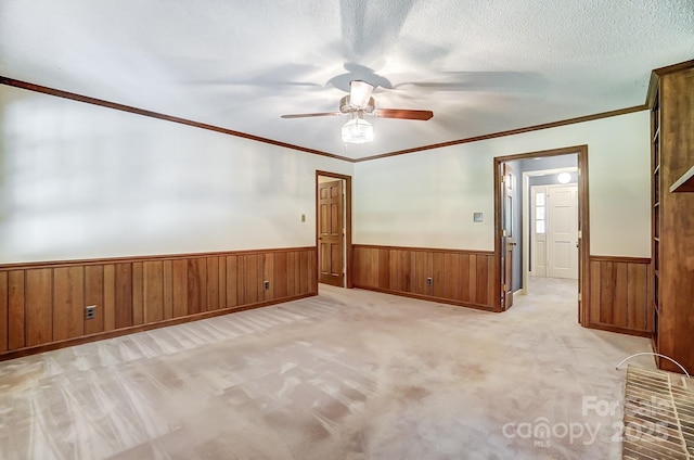 unfurnished room featuring wooden walls, light colored carpet, ceiling fan, crown molding, and a textured ceiling