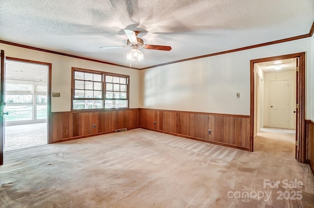 empty room with light colored carpet, ornamental molding, a textured ceiling, and wood walls