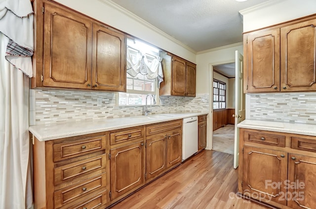 kitchen with sink, ornamental molding, plenty of natural light, dishwasher, and light hardwood / wood-style floors