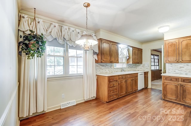 kitchen featuring crown molding, light hardwood / wood-style flooring, white dishwasher, pendant lighting, and backsplash