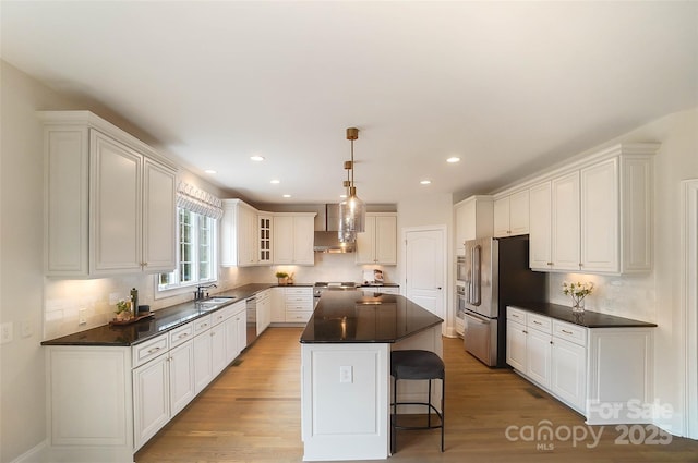 kitchen featuring white cabinetry, stainless steel appliances, a kitchen island, and wall chimney range hood