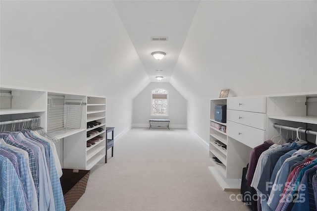 walk in closet with vaulted ceiling and light colored carpet