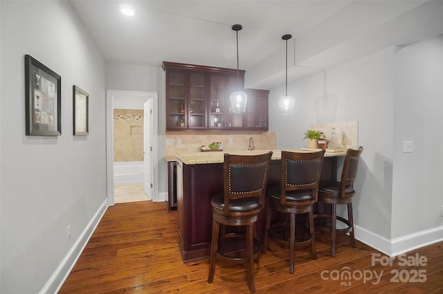 bar with sink, light stone counters, hanging light fixtures, dark hardwood / wood-style flooring, and backsplash