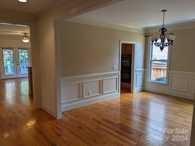 unfurnished dining area with ceiling fan with notable chandelier, plenty of natural light, light hardwood / wood-style floors, and french doors