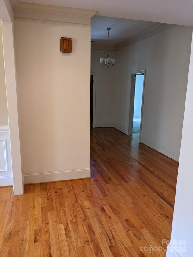 empty room with crown molding, a notable chandelier, and light wood-type flooring