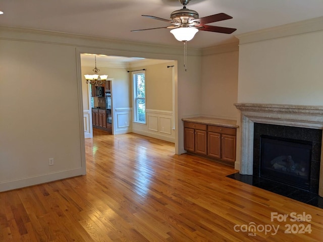 unfurnished living room with crown molding, ceiling fan with notable chandelier, and light wood-type flooring