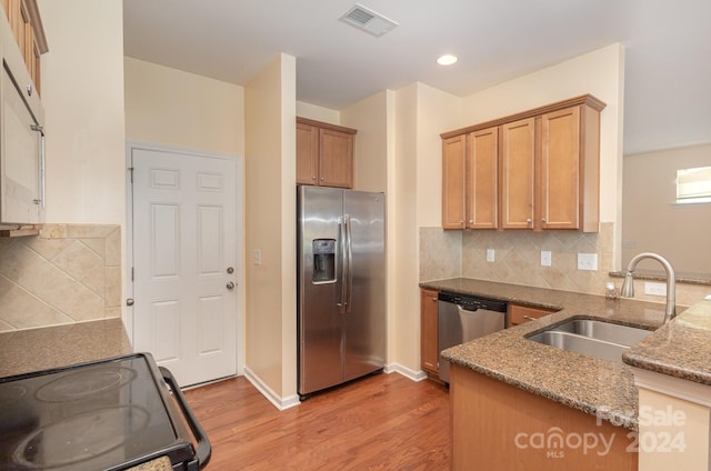 kitchen featuring appliances with stainless steel finishes, dark stone counters, sink, backsplash, and light wood-type flooring