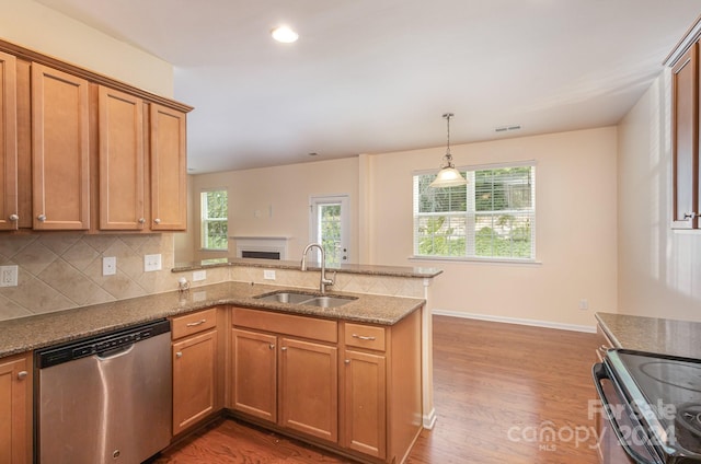 kitchen with kitchen peninsula, stainless steel appliances, light stone countertops, wood-type flooring, and sink