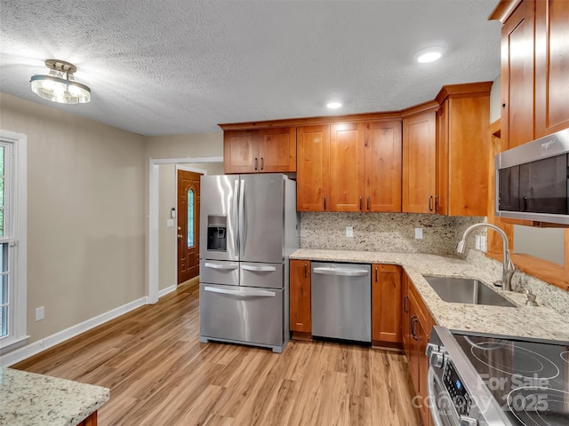 kitchen with sink, tasteful backsplash, light hardwood / wood-style flooring, stainless steel appliances, and light stone countertops