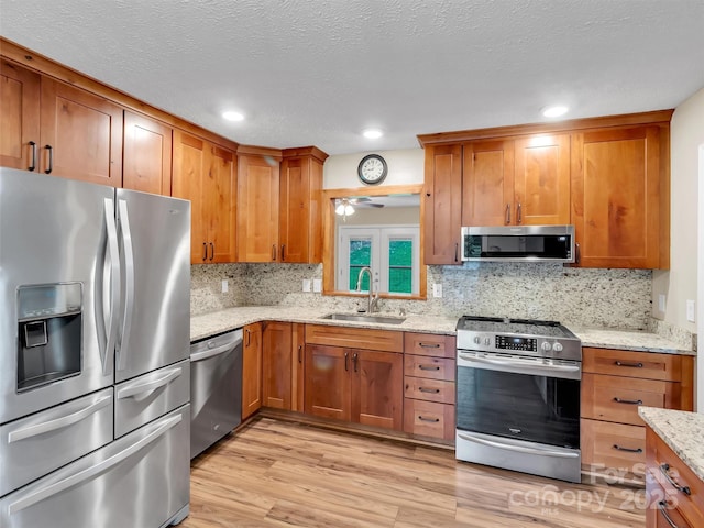 kitchen with sink, stainless steel appliances, light stone counters, tasteful backsplash, and light wood-type flooring