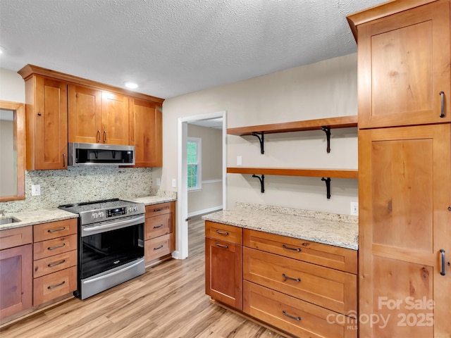 kitchen featuring appliances with stainless steel finishes, backsplash, light stone countertops, light hardwood / wood-style floors, and a textured ceiling