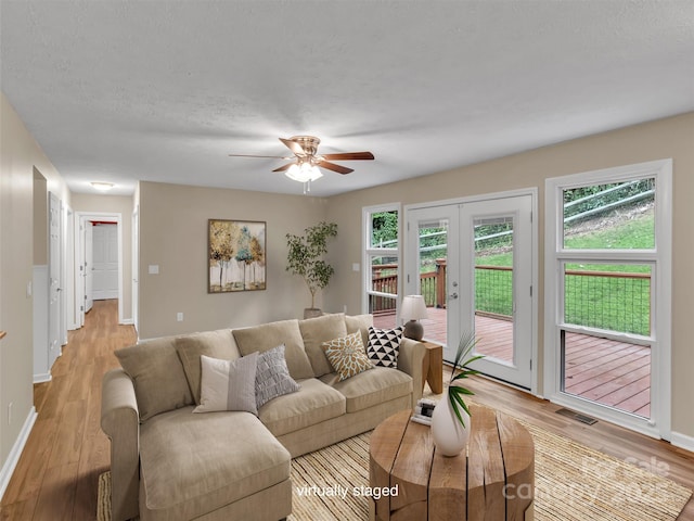 living room with ceiling fan, light hardwood / wood-style flooring, french doors, and a textured ceiling