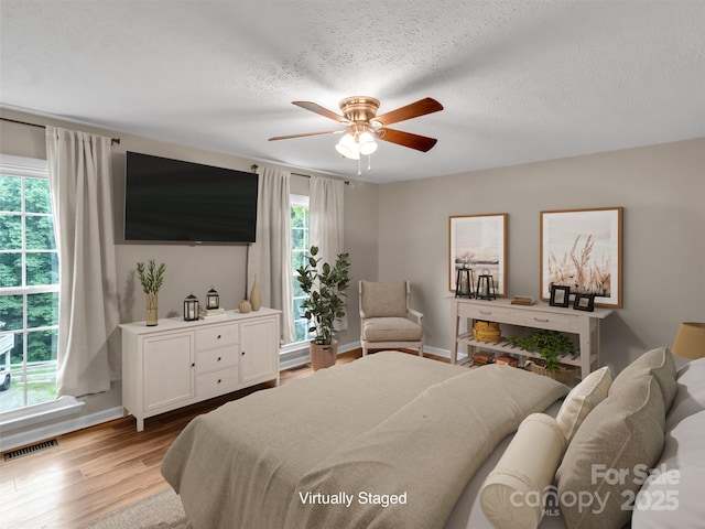 bedroom with ceiling fan, a textured ceiling, and light hardwood / wood-style floors