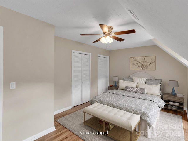 bedroom with two closets, vaulted ceiling, ceiling fan, and light wood-type flooring