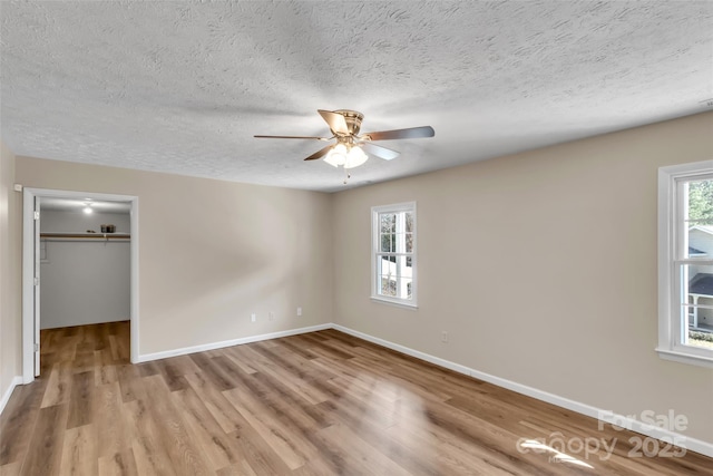 unfurnished bedroom with multiple windows, a spacious closet, light hardwood / wood-style floors, and a textured ceiling