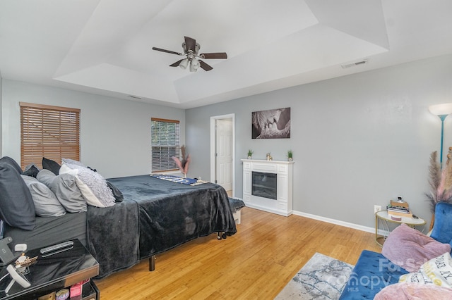 bedroom with ceiling fan, a raised ceiling, and wood-type flooring