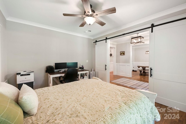 bedroom featuring crown molding, a barn door, hardwood / wood-style flooring, and ceiling fan