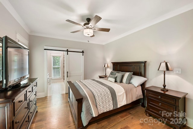 bedroom featuring light hardwood / wood-style floors, a barn door, connected bathroom, and ceiling fan