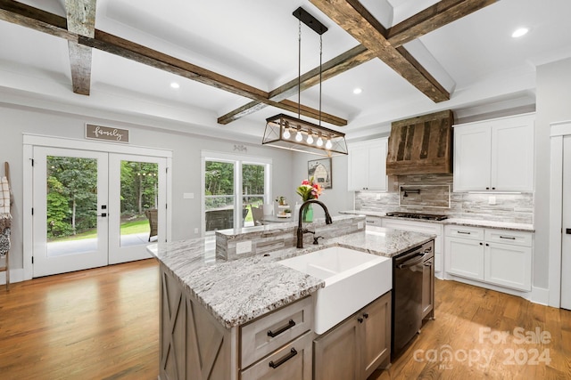 kitchen featuring beamed ceiling, pendant lighting, white cabinets, light hardwood / wood-style flooring, and a kitchen island with sink