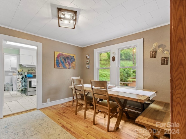 dining space with a textured wall, ornamental molding, light wood-style flooring, and baseboards