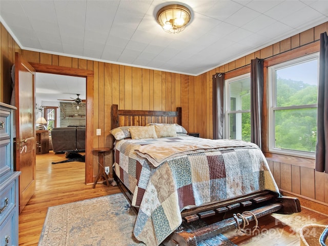 bedroom with light wood-style floors, wooden walls, and ornamental molding