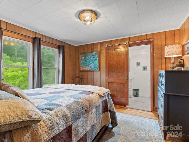 bedroom with light wood-type flooring, wooden walls, and a barn door