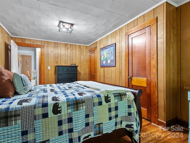 bedroom featuring wood walls, ornamental molding, and hardwood / wood-style flooring