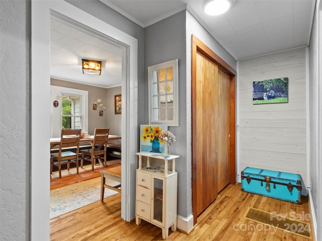 hallway featuring wood walls, crown molding, and light wood-style flooring