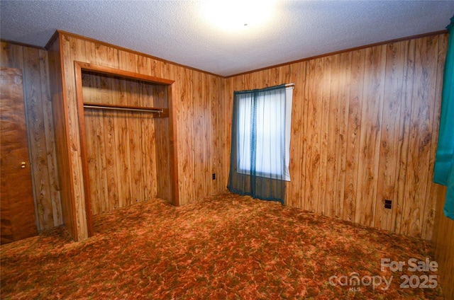 unfurnished bedroom featuring carpet floors, a closet, wooden walls, and a textured ceiling