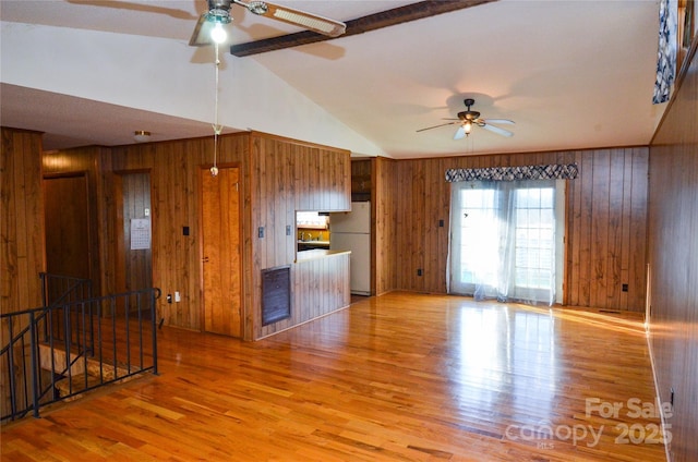 unfurnished living room with lofted ceiling with beams, ceiling fan, wooden walls, and wood finished floors