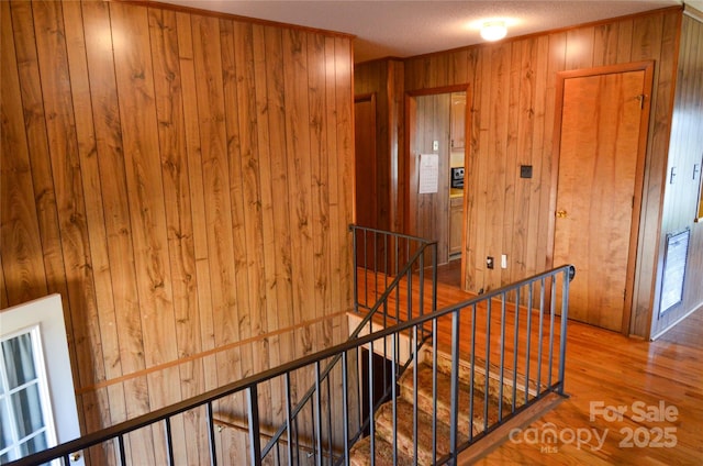 hallway featuring wood finished floors, visible vents, a textured ceiling, wooden walls, and an upstairs landing