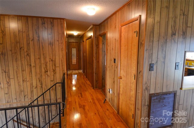 hall with crown molding, wood walls, a textured ceiling, an upstairs landing, and wood finished floors