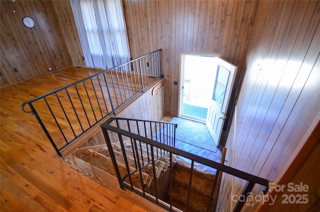 stairway featuring a healthy amount of sunlight, wooden walls, and wood finished floors