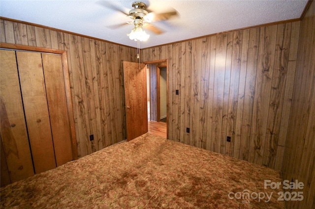 interior space featuring carpet floors, ornamental molding, wood walls, and a ceiling fan