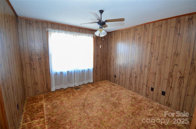 carpeted empty room featuring wood walls and a ceiling fan