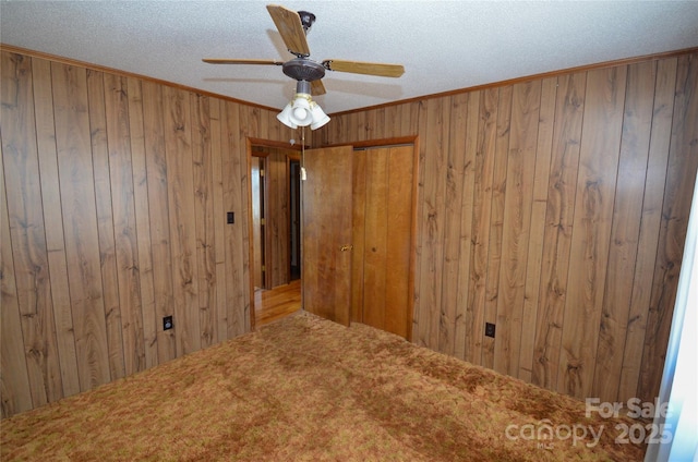 carpeted empty room featuring a textured ceiling, crown molding, a ceiling fan, and wooden walls