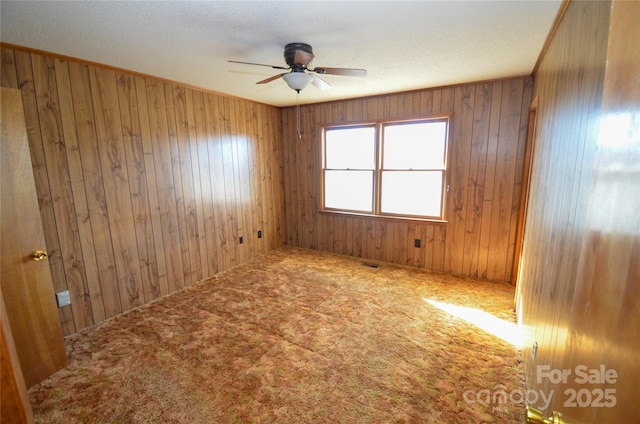 carpeted empty room featuring wood walls, ceiling fan, ornamental molding, and a textured ceiling